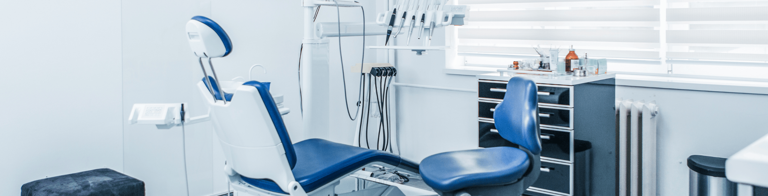 An empty, modern dental clinic with a blue and white dental chair positioned in the center.