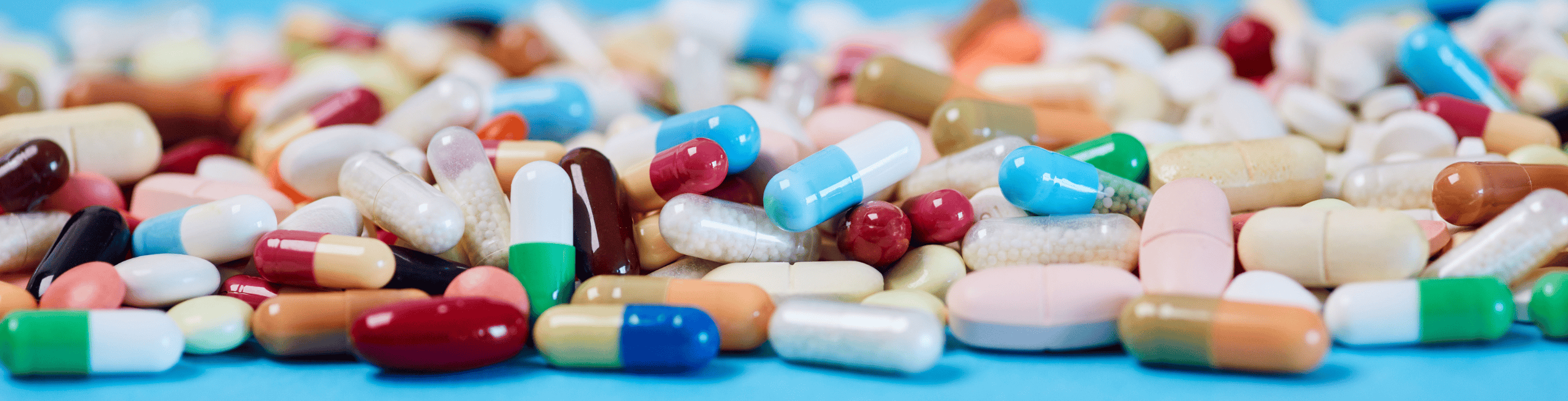 Assorted pharmaceutical pills and capsules spread out on a blue surface